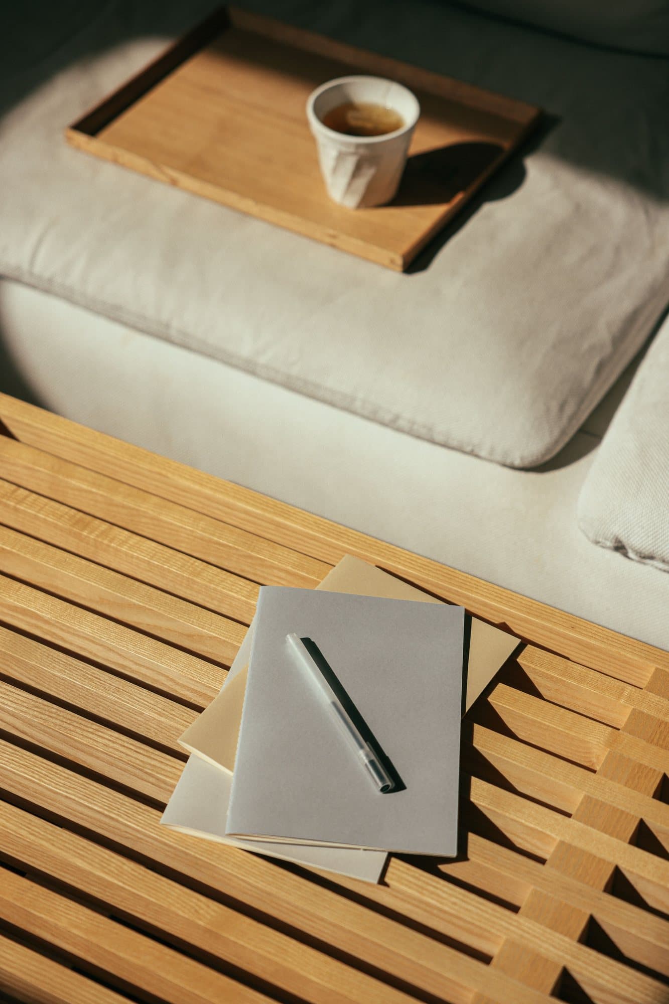 Thé et carnet posés sur une table basse en bois, lumière du matin